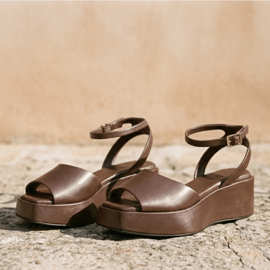 Braune Sandalen mit einer Plateausohle stehen auf einem Steinboden.