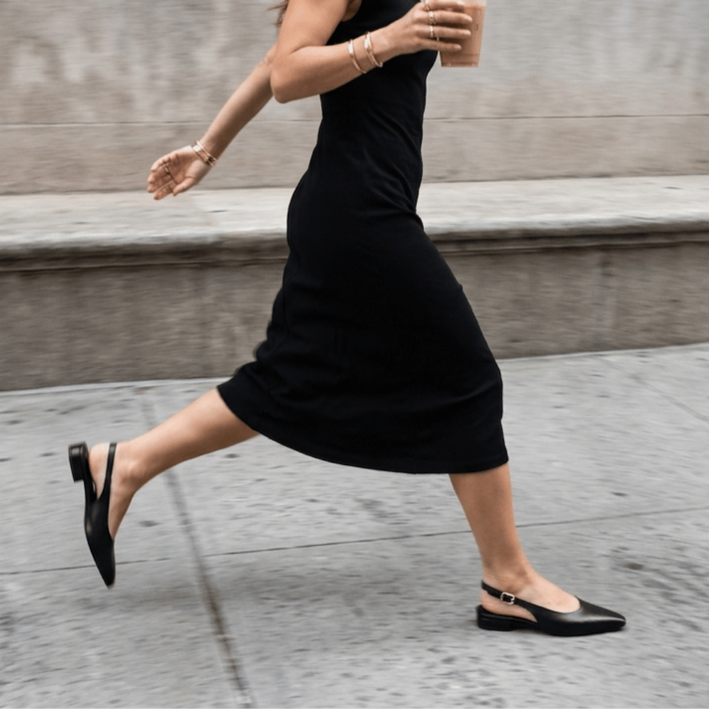 Eine Frau trägt ein schwarzes Stoffkleid und schwarze Slingbacks. dazu trägt sie goldenen Schmuck.